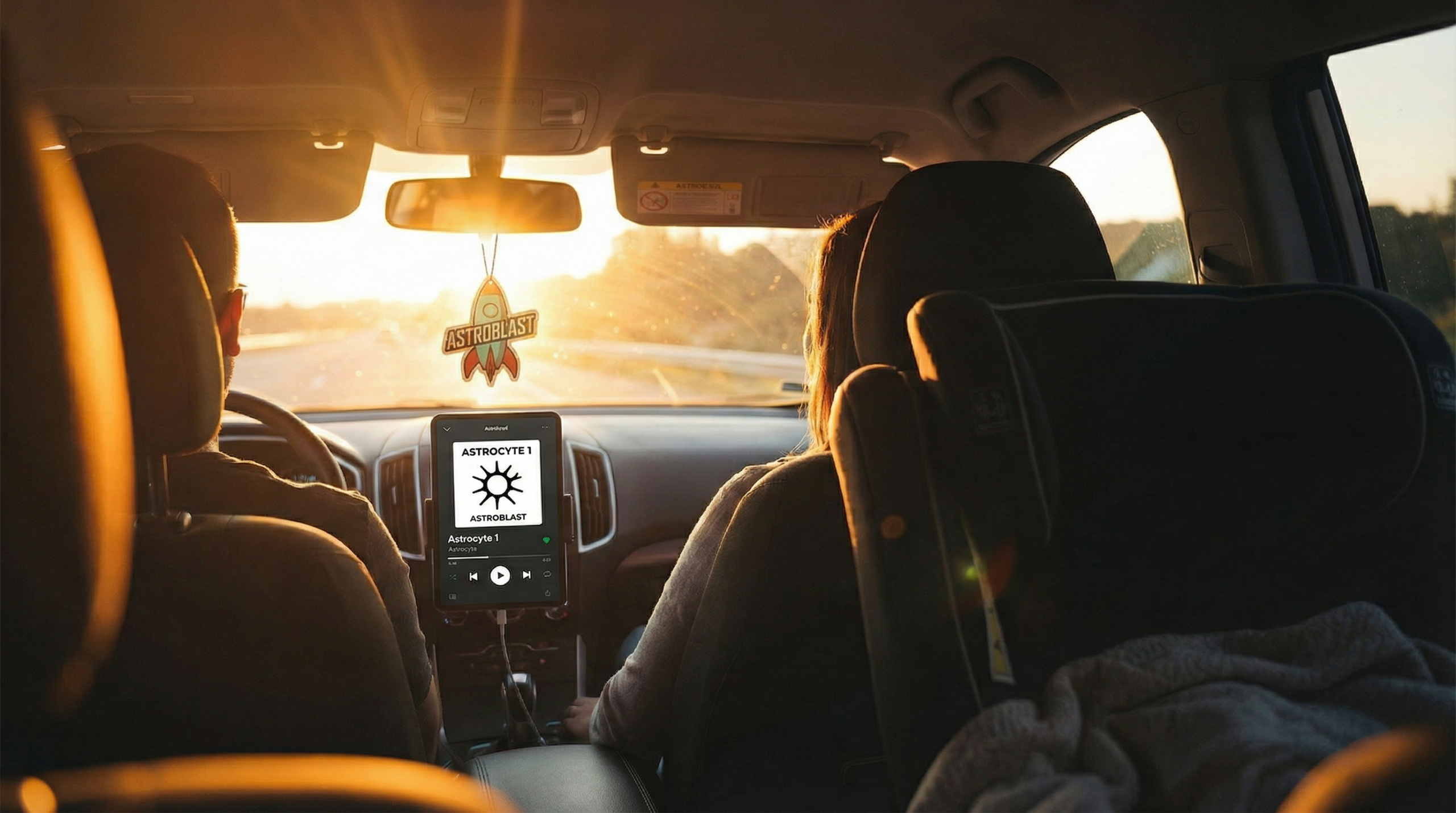 夕焼けの中を走る車内、ダッシュボードにAstrocyte 1のアルバムアートが表示されている